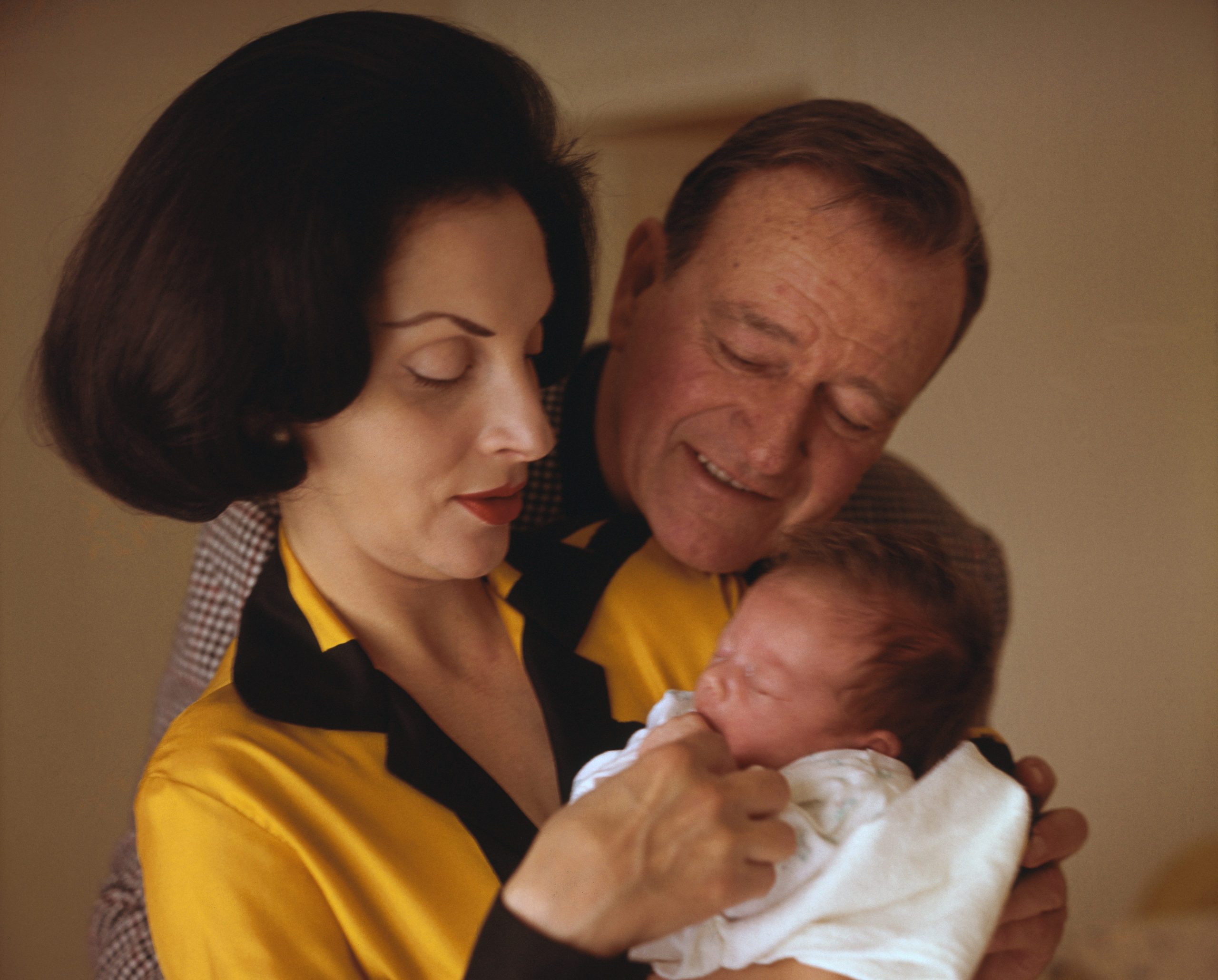 (Original Caption) Newport Beach, California: Actor John Wayne nuzzles up to his new baby, Marisa Carmela, at Wayne's home here March 12. Helping to hold the baby is the proud mother, Pilar, who gave birth to the young Wayne on February 22nd. Wayne just finished Eldorado for Paramount and will spend some time with his wife and daughter.