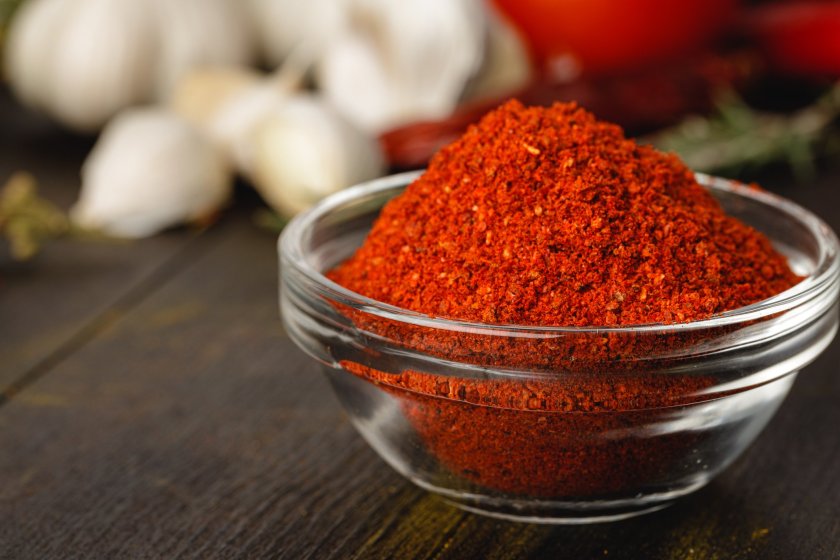 Red chili spice in glass bowl with herbs on dark table