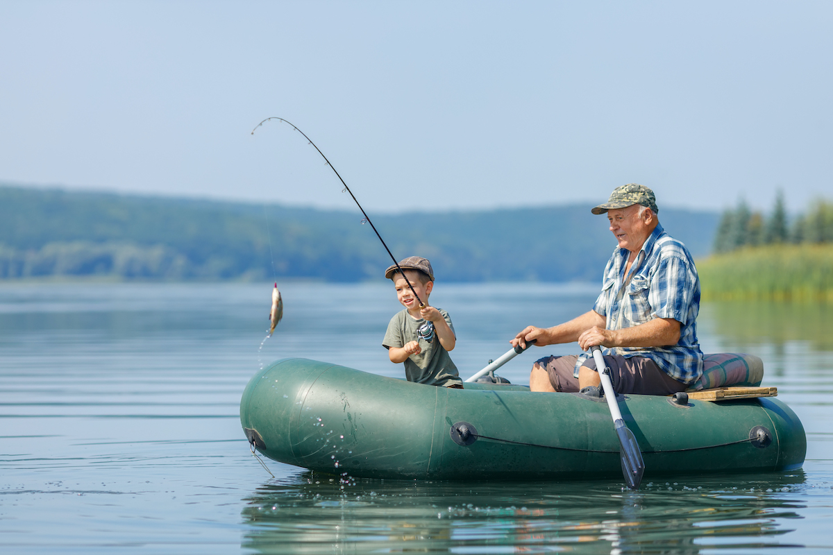smiling little boy with elderly grandfather together fishing on the river. Concept of connection between generations