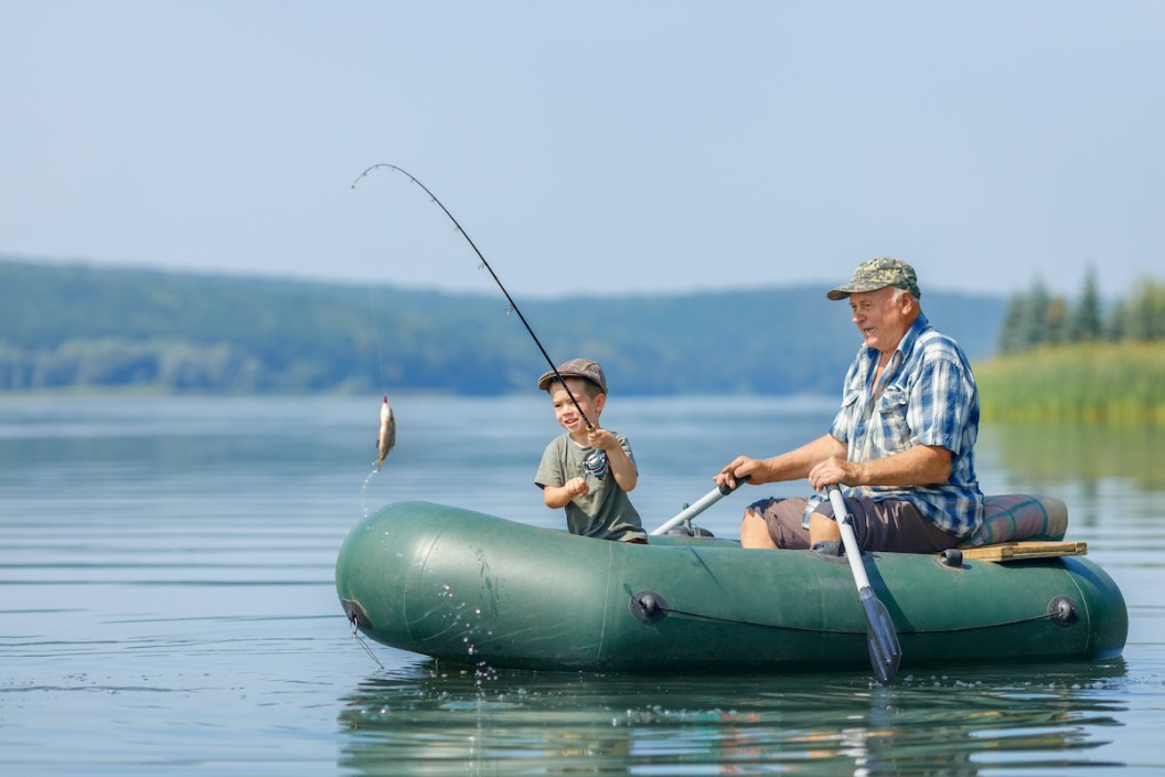 smiling little boy with elderly grandfather together fishing on the river. Concept of connection between generations