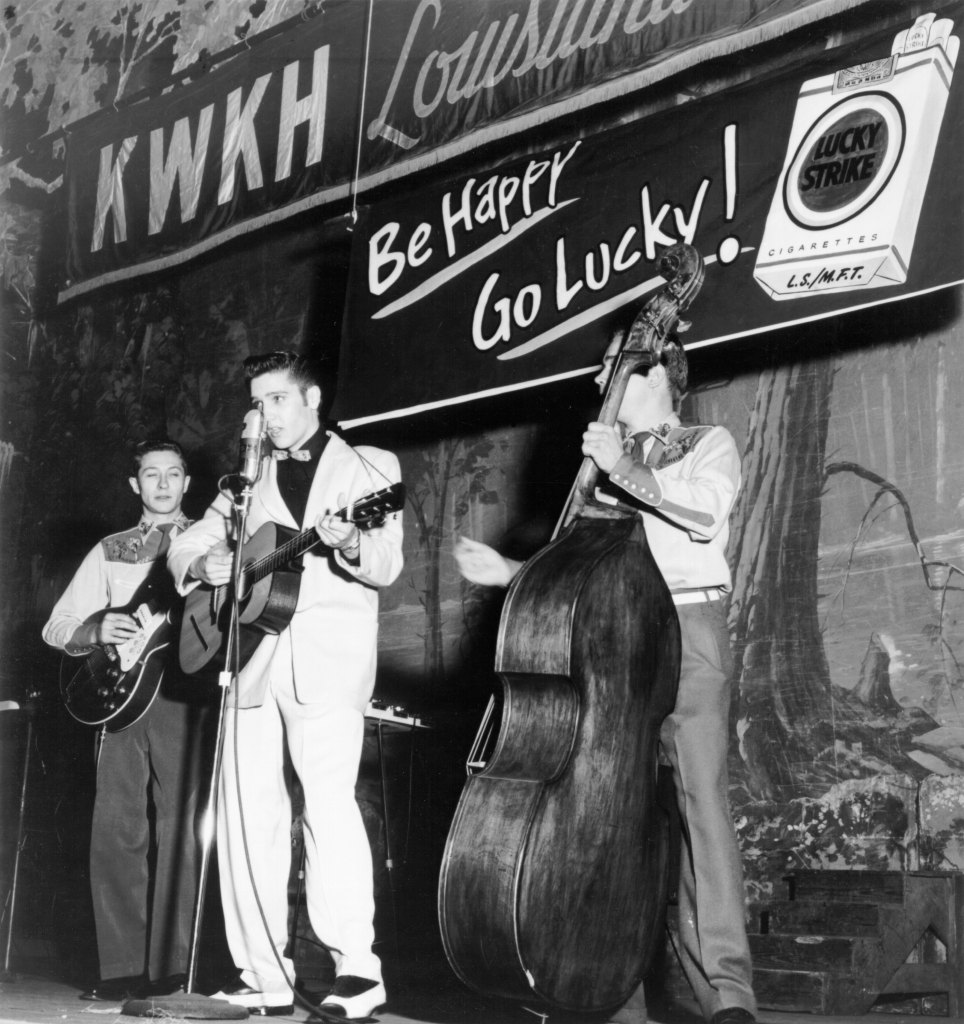 SHREVEPORT, LA - OCTOBER 16: Singer Elvis Presley joins his guitar player Scotty Moore (left) and bass player Bill Black on a weekly broadcast of "Lousiana Hayride" at the Shreveport Auditorium just three months after Elvis left home for the first time on October 16, 1954 in Shreveport, Lousiana. 