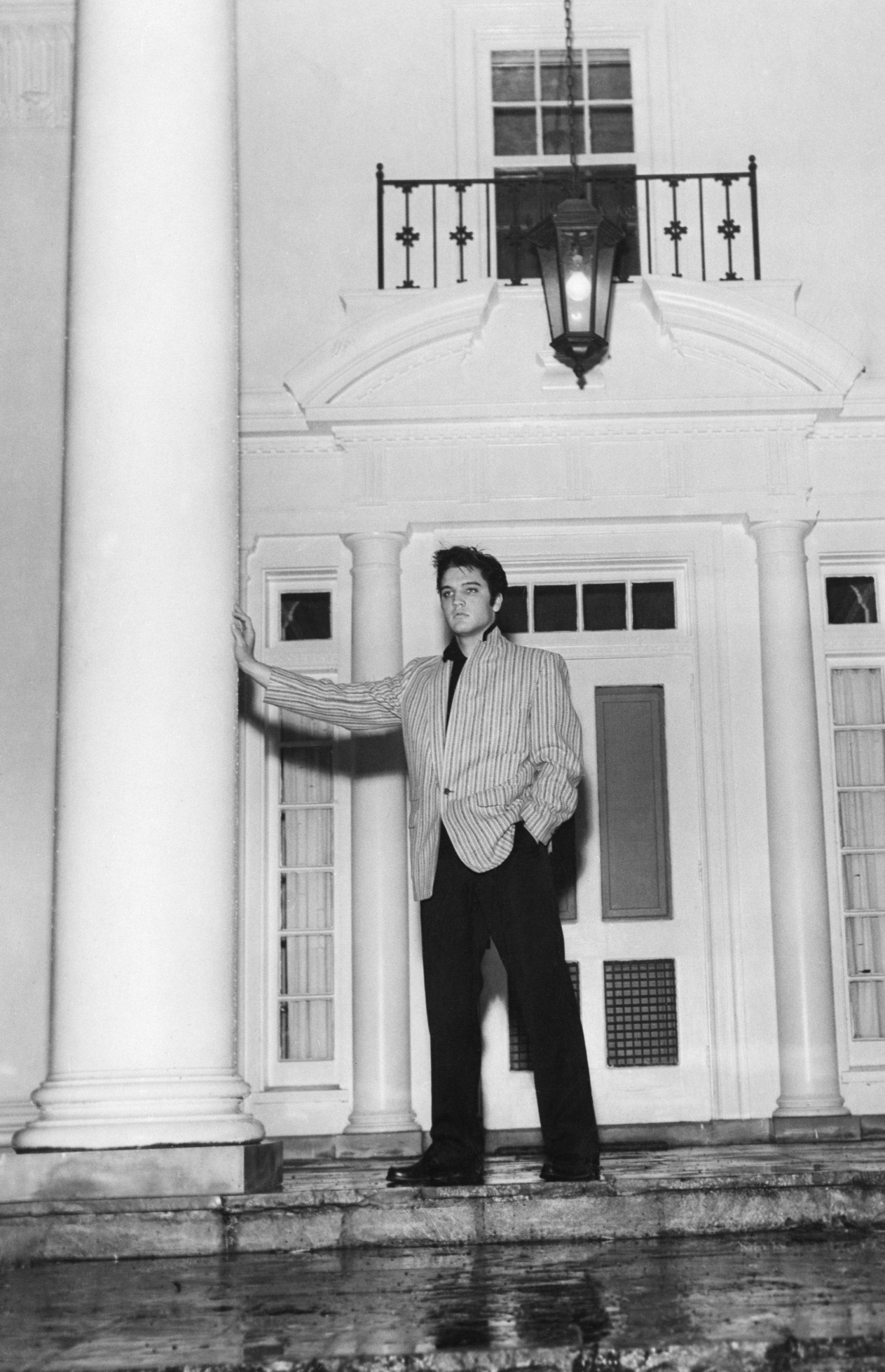 (Original Caption) 3/26/1957-Memphis, TN-A thoughtful Elvis Presley leans against a massive pillar on the front porch of his traditional southern-style home, "Graceland," at Whitehaven, near Memphis.