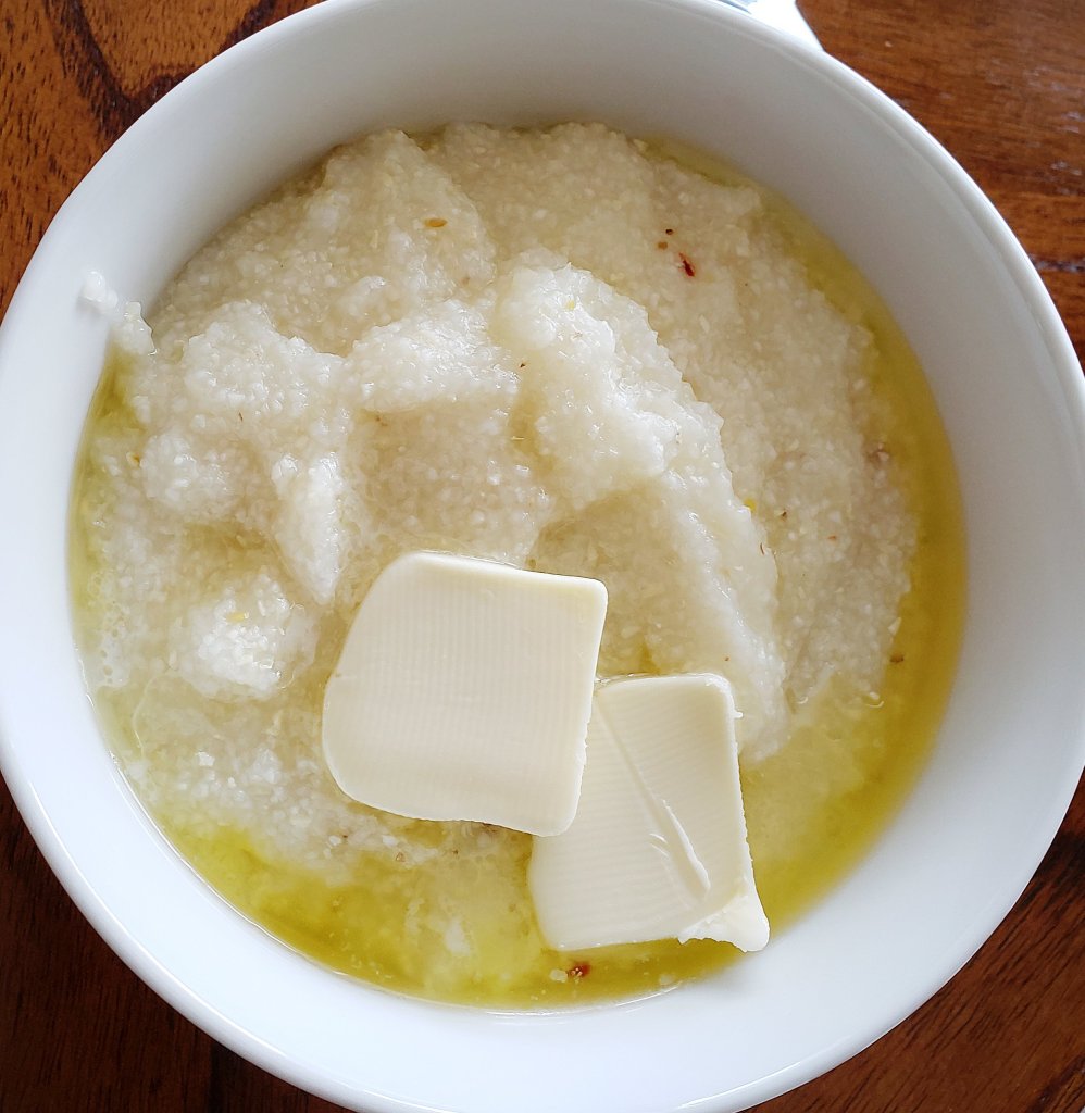 Bowl of grits with melting butter and crushed red pepper on wooden table.