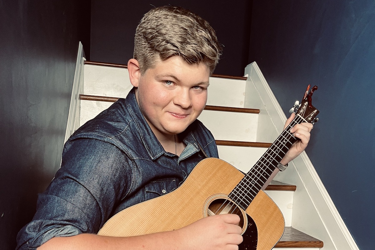 Alex Miller strums his guitar while seated on a flight of stairs.
