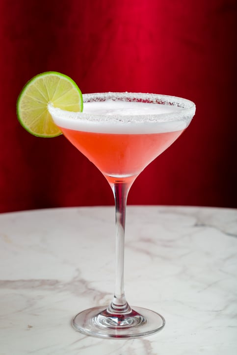 cosmopolitan cocktail with lime and salted rim on marble table and red curtain behind