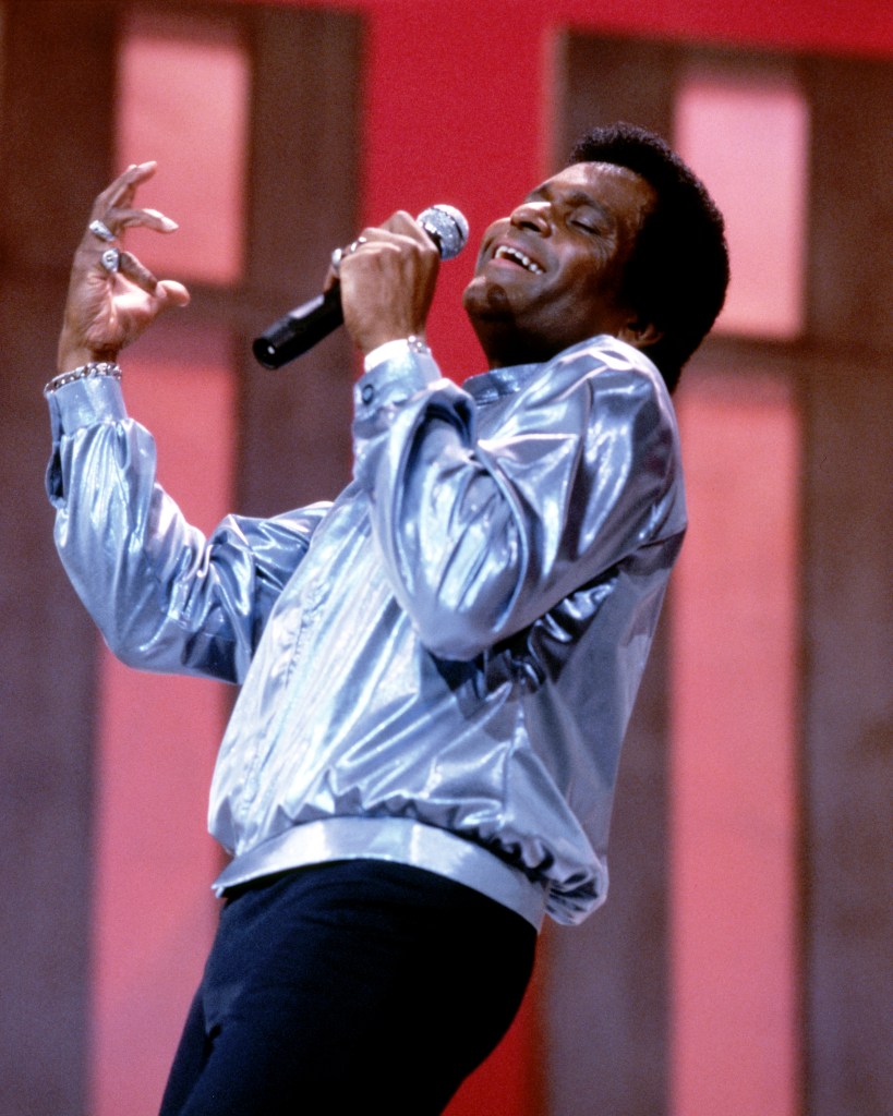 Charley Pride, US Country music singer, wearing a silver jacket and holding a microphone during a live concert performance, circa 1975.