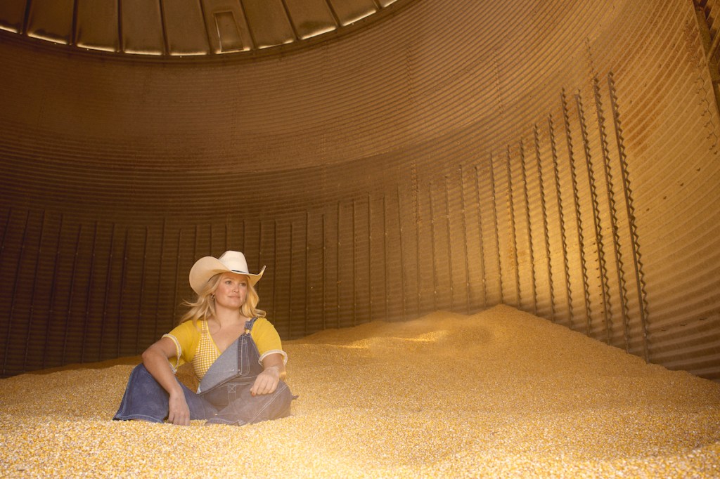 Hailey Whitters poses in cowboy hat and overalls
