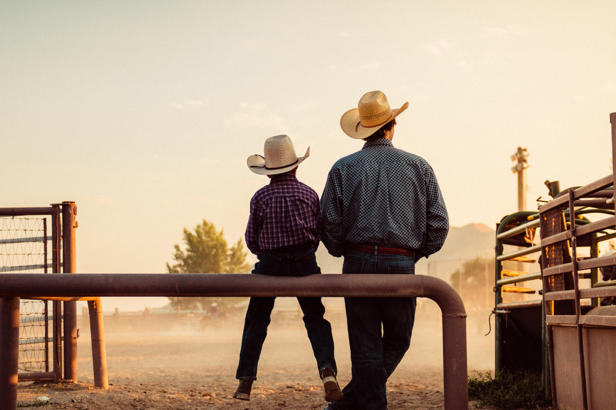 Father and son sitting by rodeo arena at sunrise