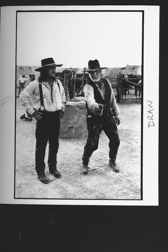 (L-R) C/W singer Kenny Rogers shows of his six-gun shooting style to singer Travis Tritt, (both in Western costumes), outside on set during break in the filming of TV movie Rio Diablo on location. 