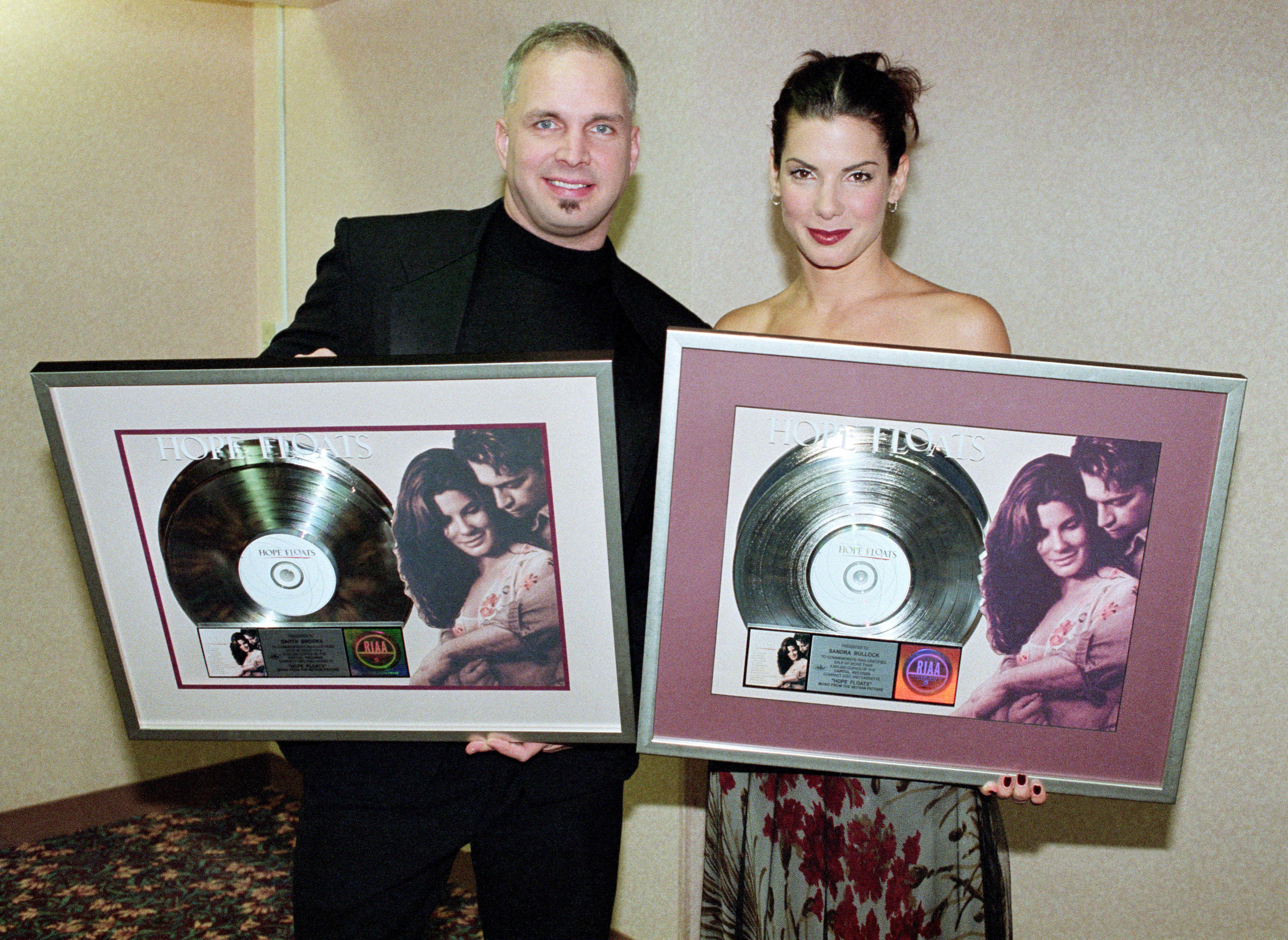 LOS ANGELES, CA - JANUARY, 1999: (L-R) American singer and songwriter Garth Brooks and American actress and producer Sandra Bullock pose for a portrait and hold a commemorative record for two million copies sold of the soundtrack for the movie "Hope Floats" circa January, 1999 in Los Angeles, California. 