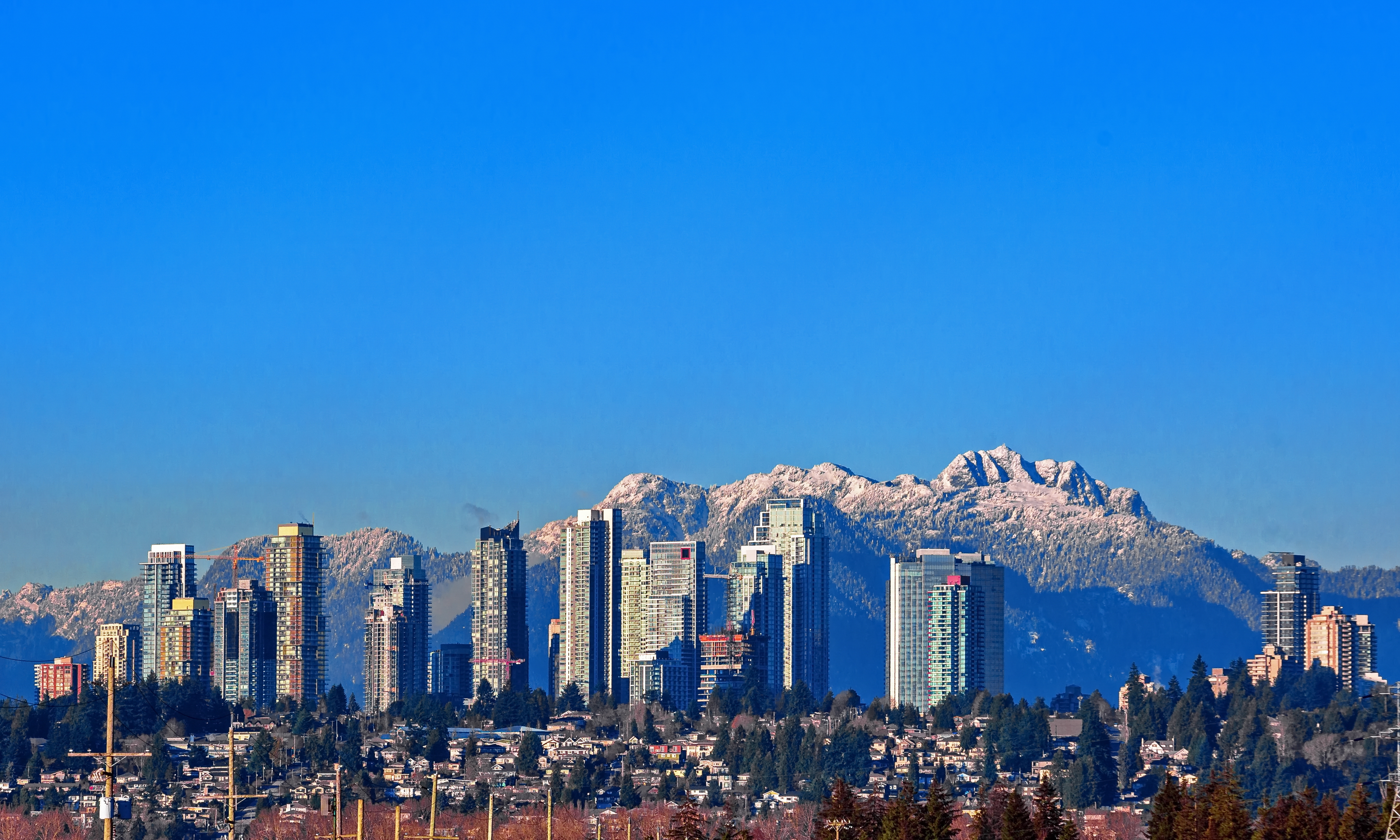 New residential area of high-rise buildings in the city of Burnaby, construction site in the center of the city against the backdrop of snow covered mountain range and blue sky