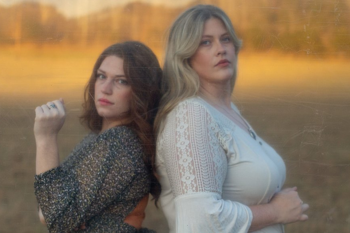 The Local Honeys, Linda Jean Stokley (guitar, fiddle, vocals) and Montana Hobbs (banjo, vocals), pose back to back