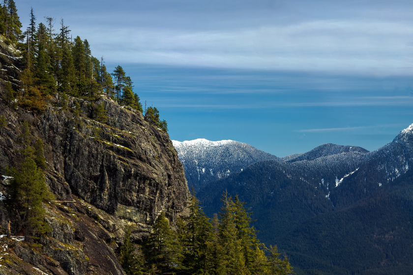 Winter forest in the mountains over Vancouver and snow-capped peaks on the background of blue cloudy sky. The picture was taken from the cabin of the sky ride going to the ski slopes of the Grouse Mountains