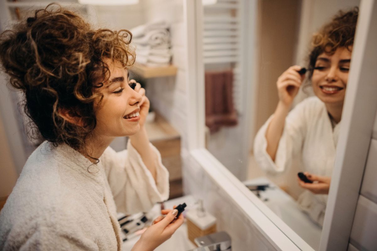 woman putting on mascara in front of mirror