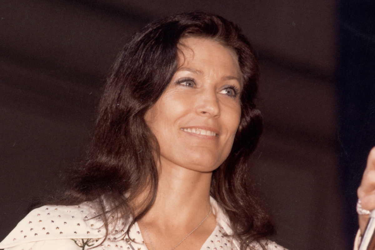 American country music singer and guitarist Loretta Lynn smiles as she looks at an unidentified person off-camera who holds a microphone, late 1970s. (Photo by Hope Powell/Hulton Archive/Getty Images)