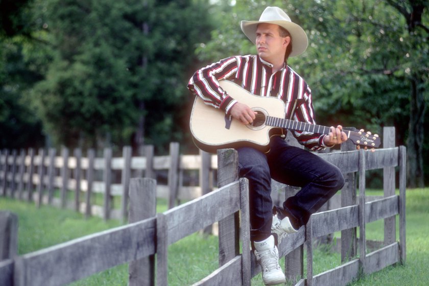 NASHVILLE, TN - AUGUST 15: Country music star Garth Brooks poses for a portrait session on a fence wearing a cowboy hat and playing a Takamine acoustic guitar on August 15, 1991 in Nashville, Tennessee.
