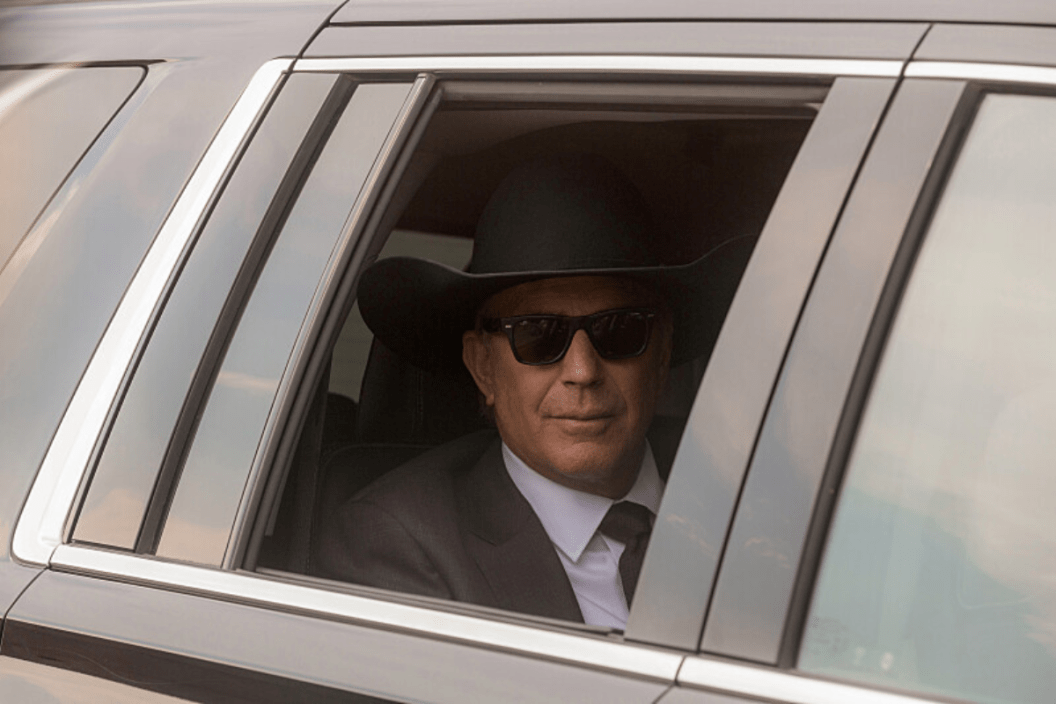 John Dutton rides in the back seat of a car in a scene from 'Yellowstone'