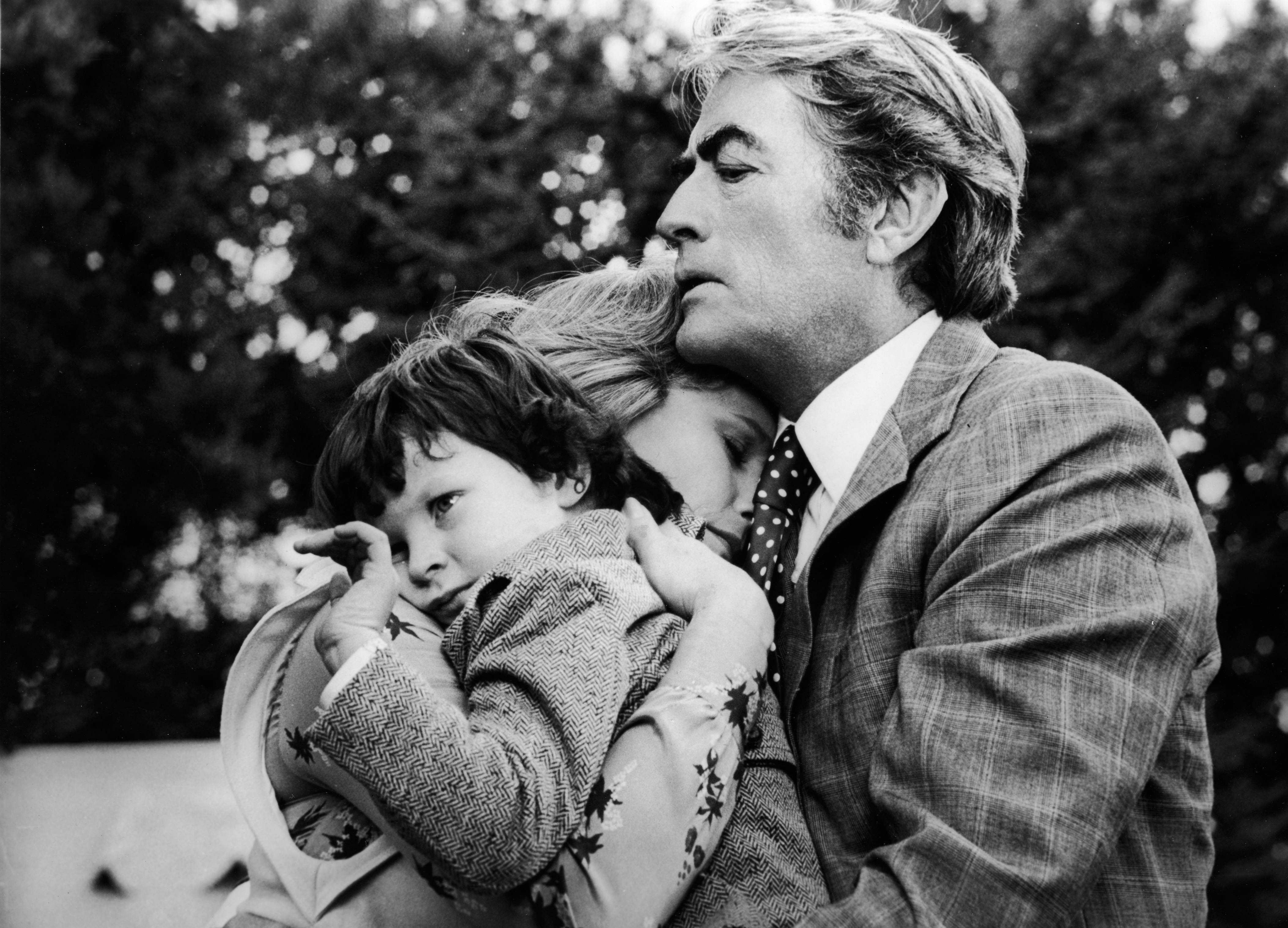 Actors Gregory Peck and Lee Remick embrace child Harvey Stephens in a still from the film, 'The Omen,' directed by Richard Donner, 1976.