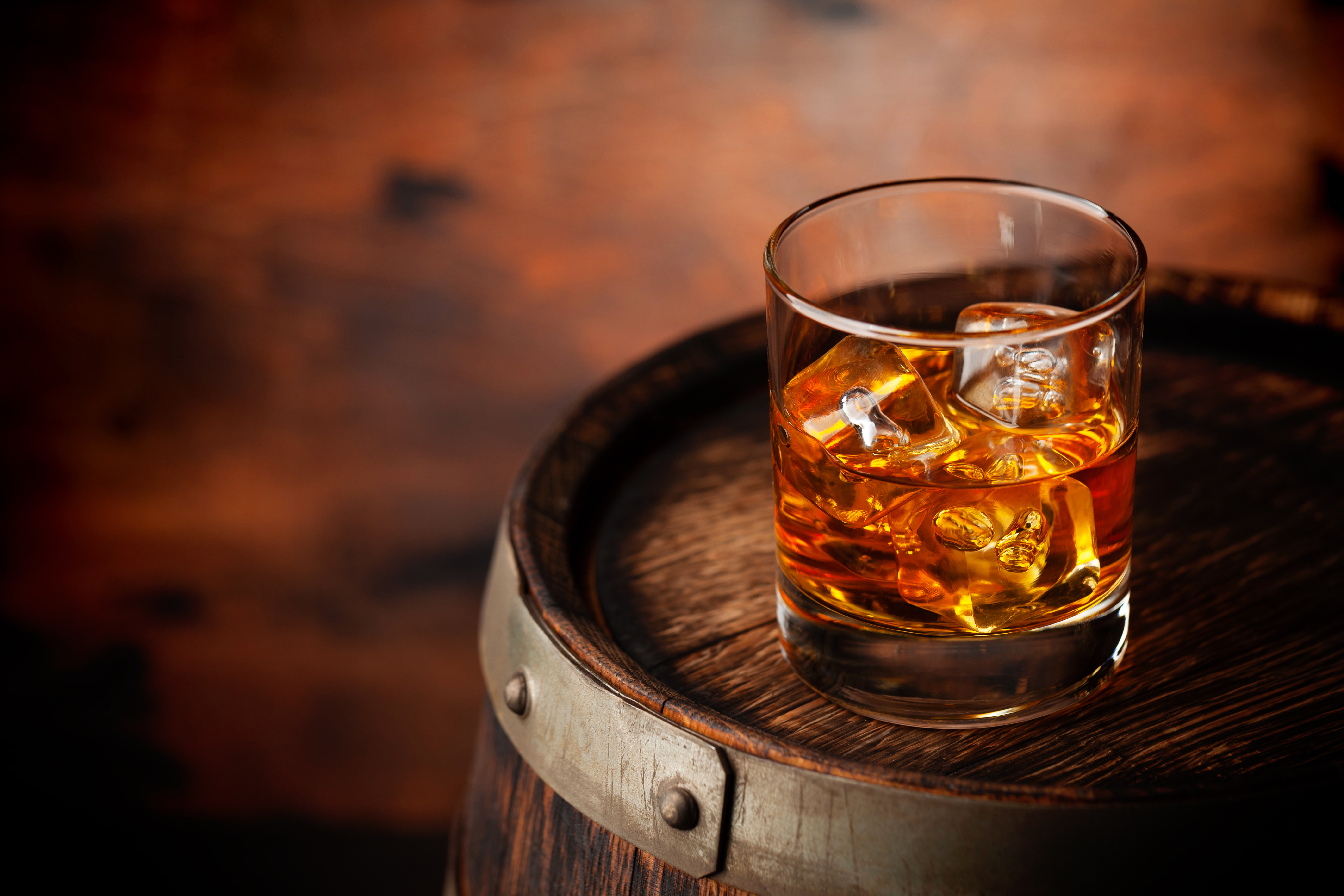 Glass of whiskey with ice cubes on the old barrel. With copy space on wooden background