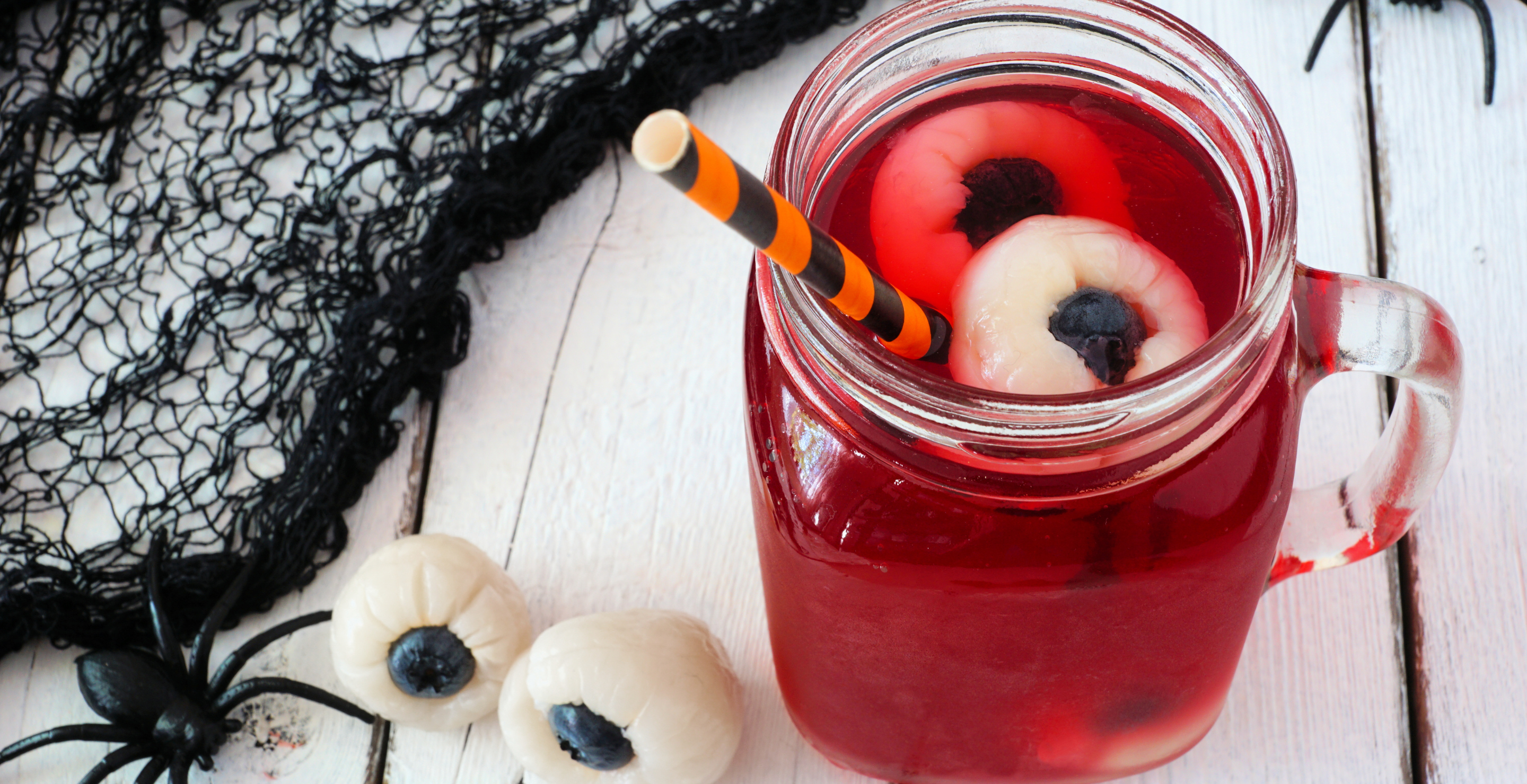 Creepy Halloween eyeball fruit punch in a mason jar against a white wood background
