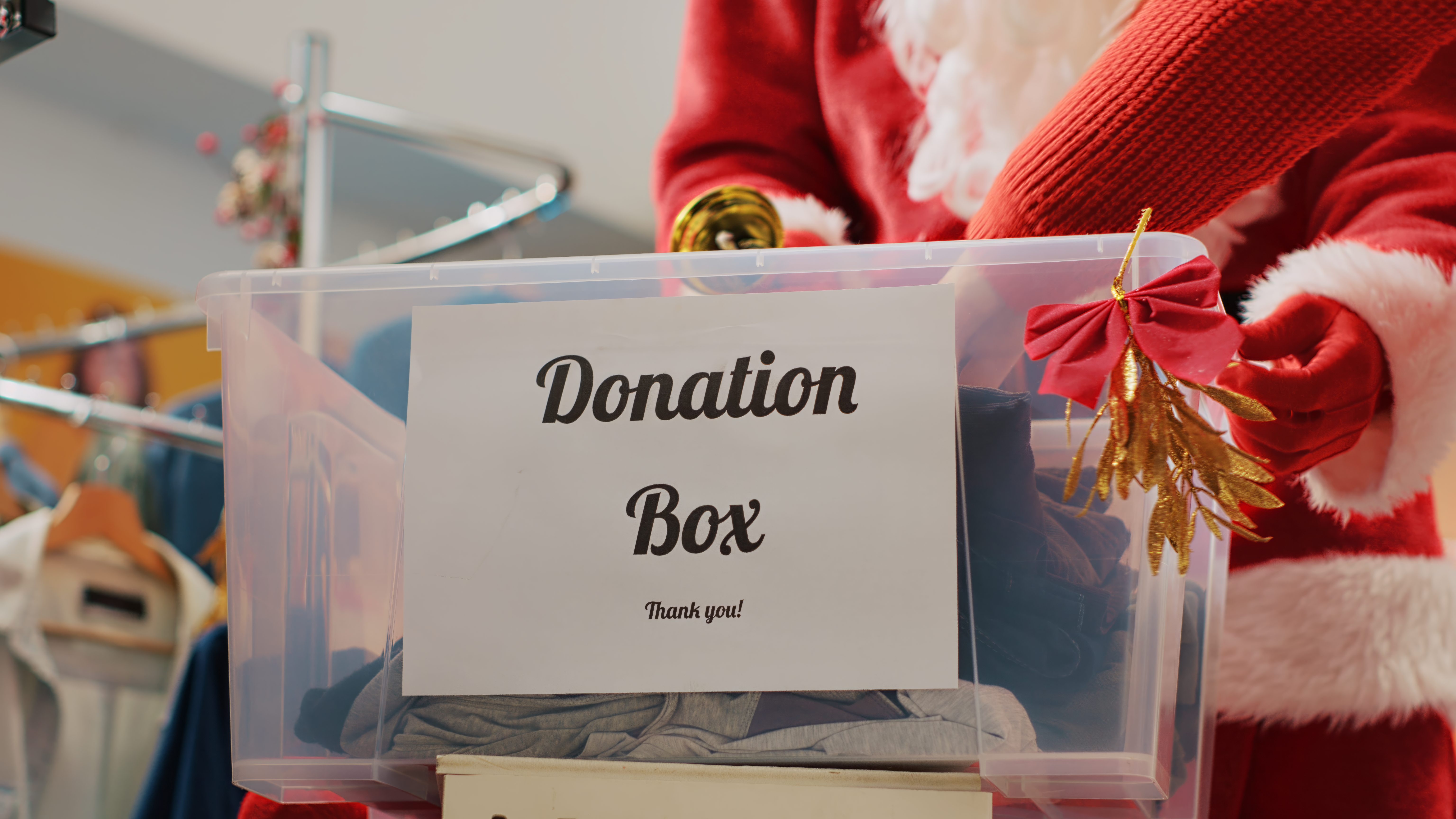 Close up shot of donation box in fashion shop set up for humanitarian help during Christmas holiday season. Worker dressed as Santa Claus collecting unneeded clothes from generous clients