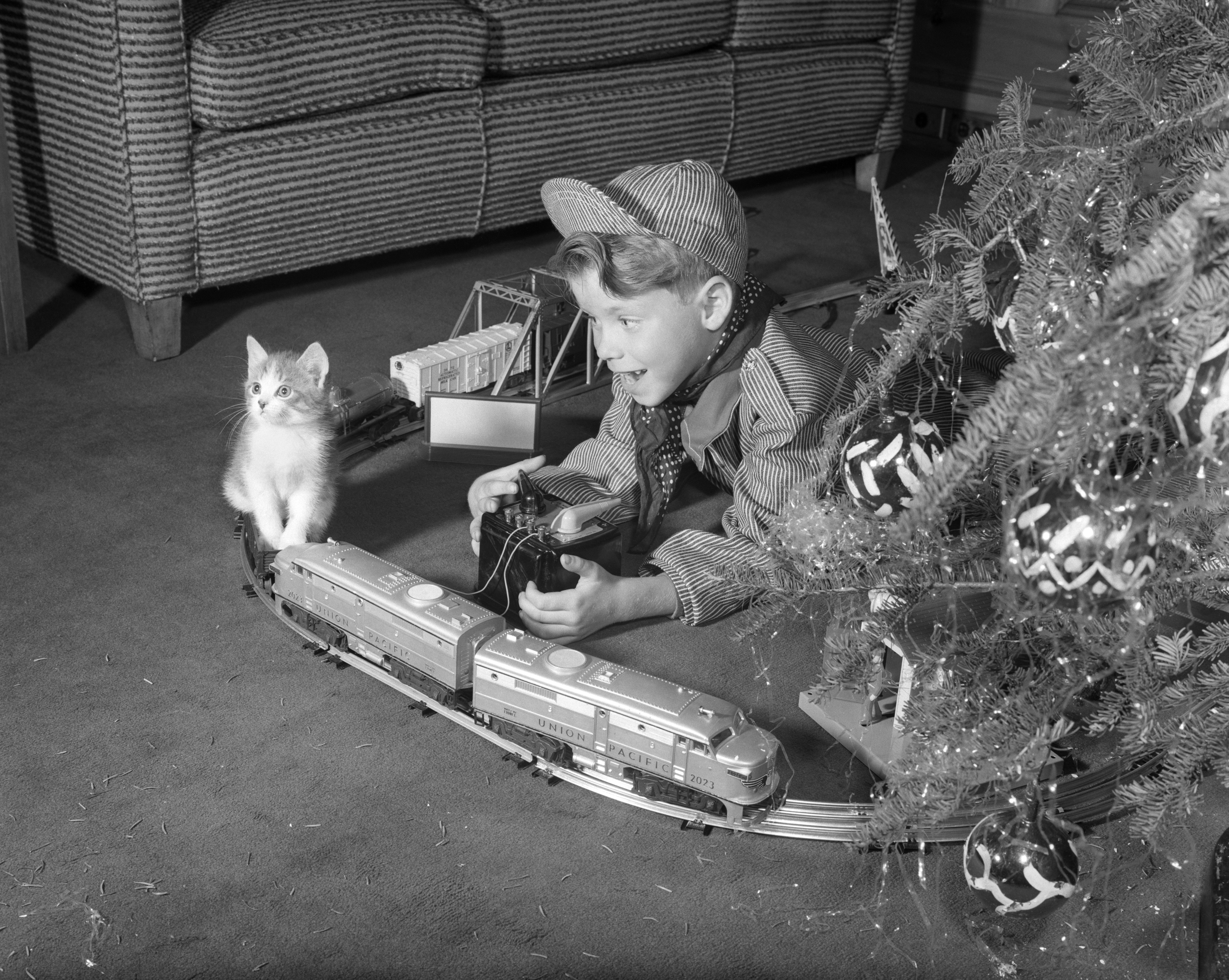 1950s BOY IN ENGINEER OUTFIT WITH KITTEN PLAYING WITH ELECTRIC TRAIN BY CHRISTMAS TREE (Photo by Debrocke/ClassicStock/Getty Images)