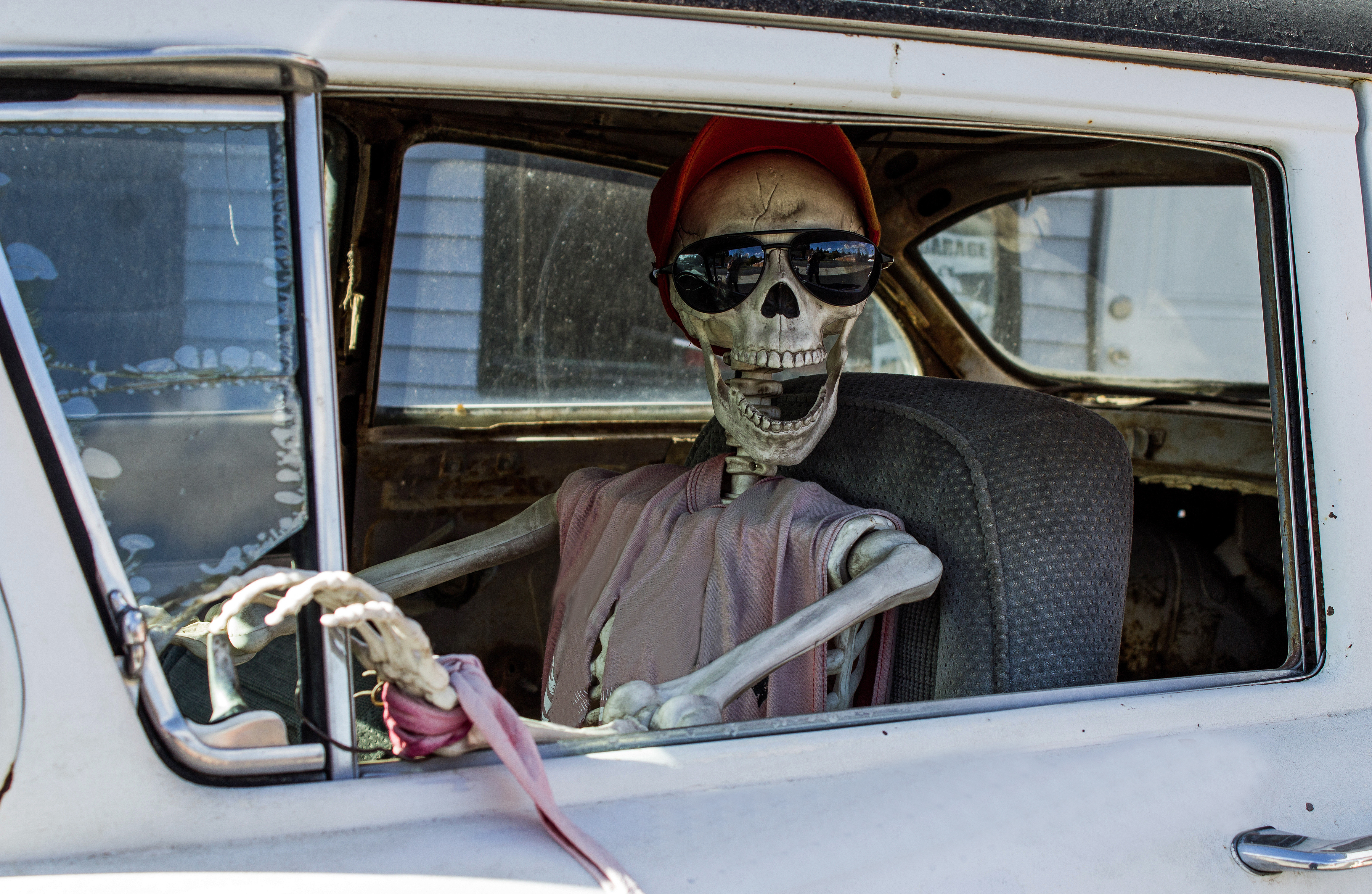 Smiling Skeleton in Sunglasses and a Red Baseball Cap Driving a Car