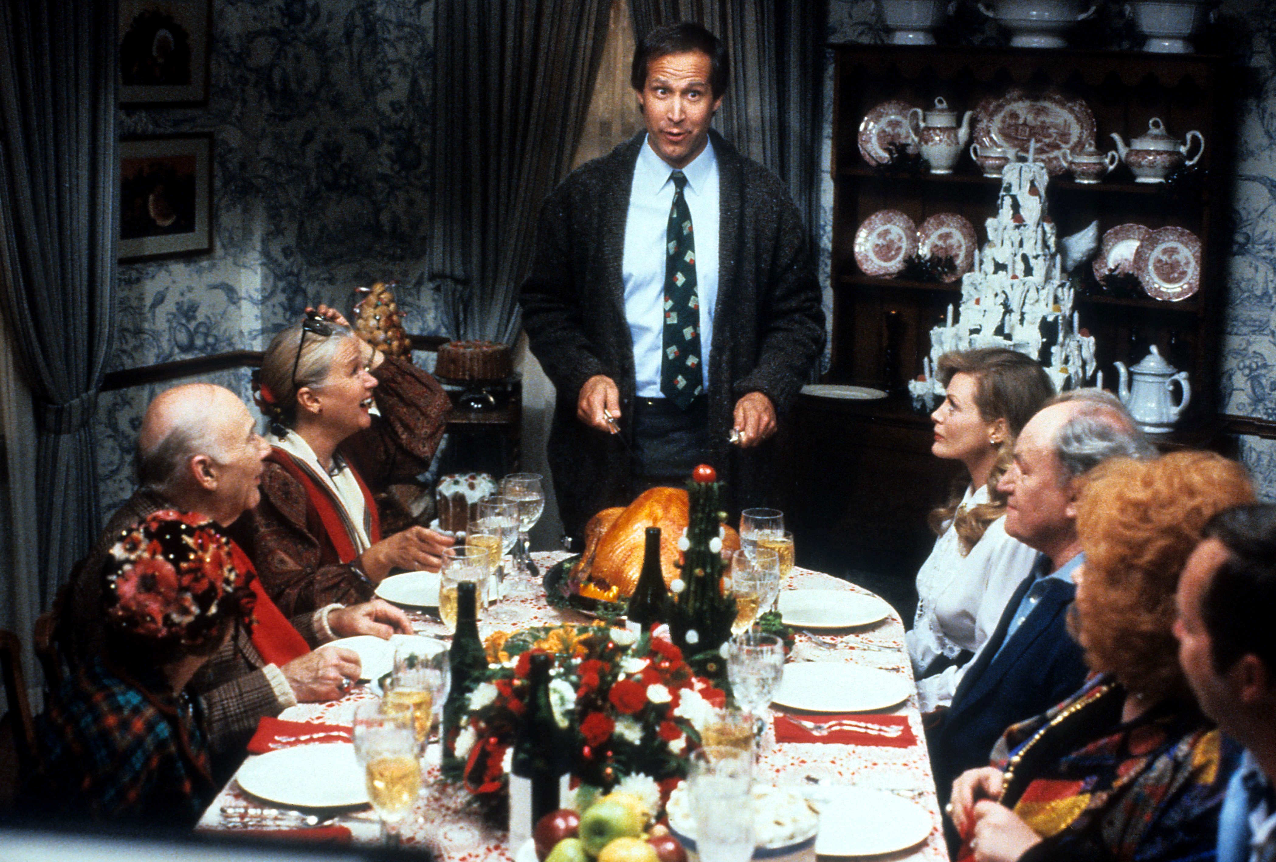 Chevy Chase stands at the head of the table in a scene from the film 'Christmas Vacation', 1989.