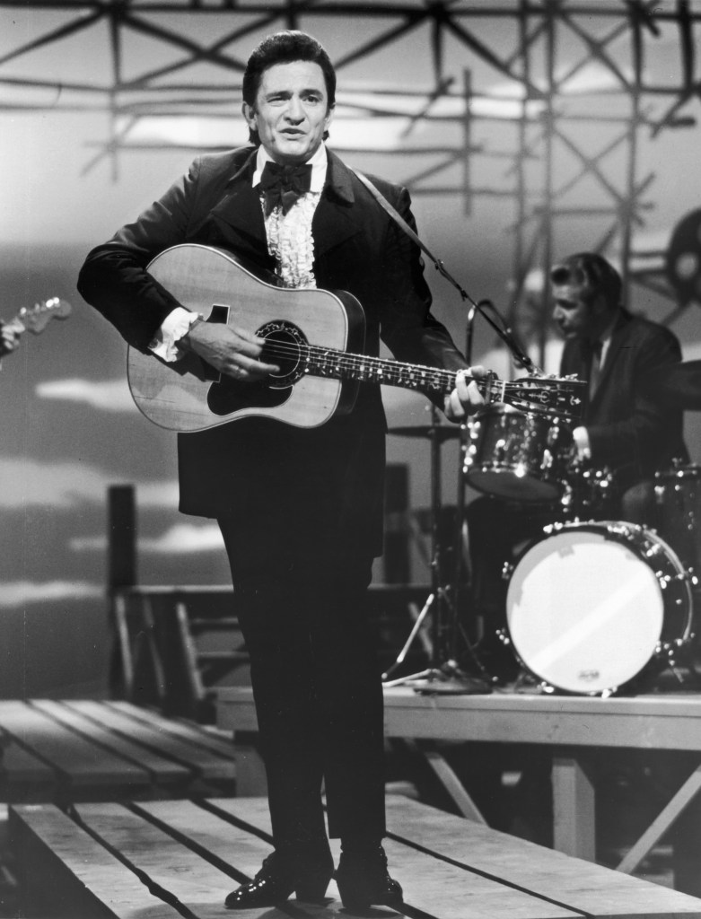 circa 1965: Full-length image of American country singer and musician Johnny Cash (1932 - 2003), wearing a tuxedo, performing with a guitar on stage during a television appearance.
