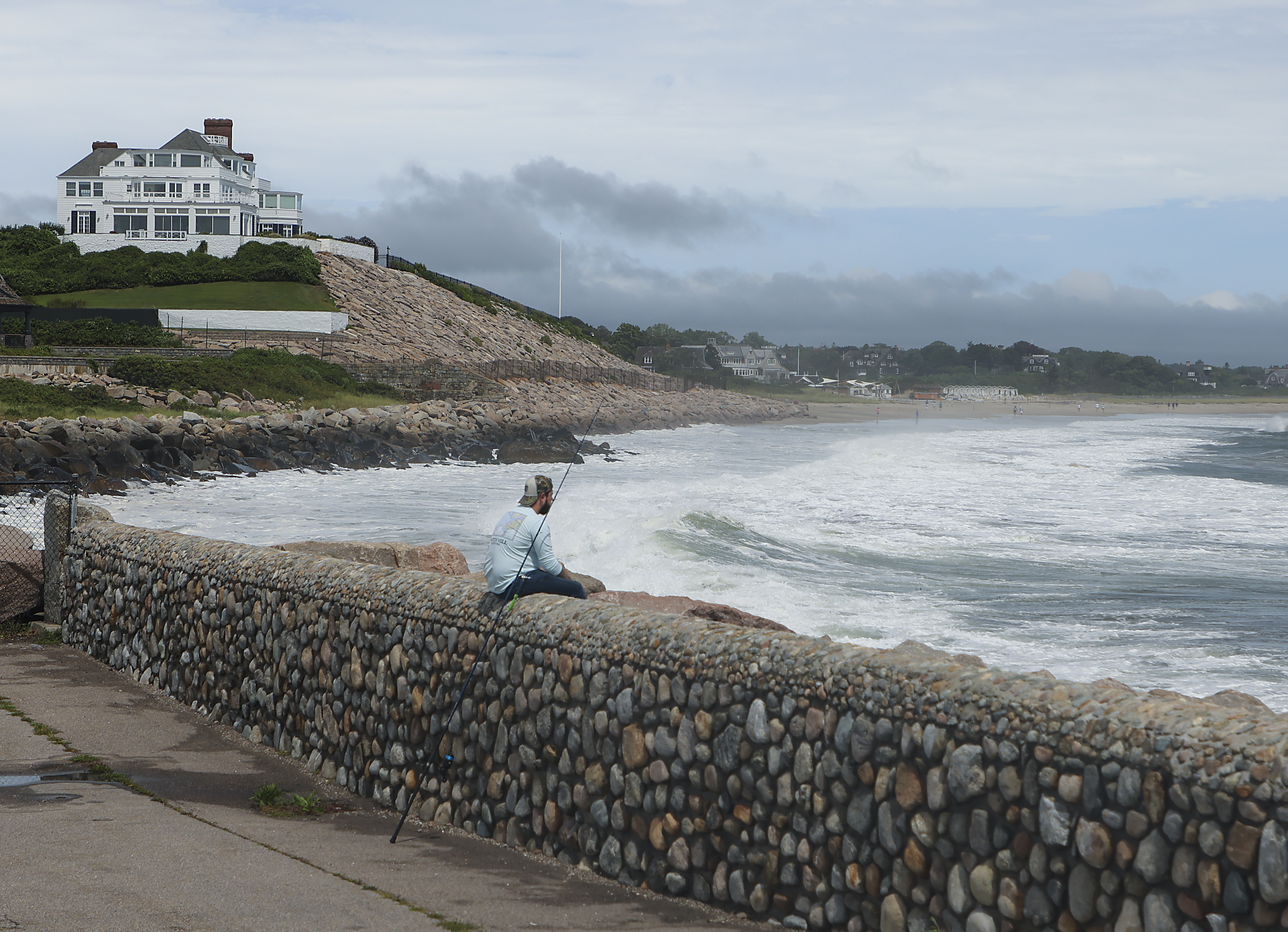 Westerly, RI - August 22: A man fishes at the Watch Hill Lighthouse for stripped bass with home of Taylor Swift in the background during the eye of the Tropical Storm Henri in Westerly, RI on Aug. 22, 2021.