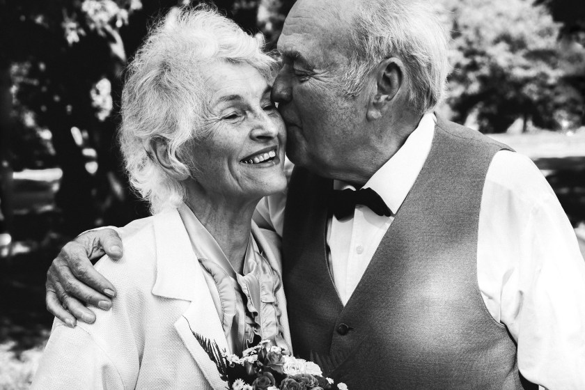Old couple is walking in the green park. Grandmother and grandfather at their golden wedding anniversary celebration. Fifty years together love story. Grandma and grandpa kissing. Black and white.