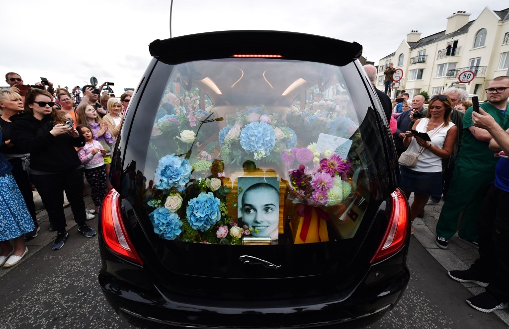 BRAY, IRELAND - AUGUST 8: Crowds of people line the street as the hearse carrying Sin&eacute;ad O'Connor's coffin passes by her former home on the seafront on August 8, 2023 in Bray, Ireland. The public lined the streets of Bray today as the funeral cortege of Sin&eacute;ad O'Connor passed through the town where she lived for 15 years. The iconic Irish singer known for her hit single "Nothing Compares 2 U" passed away at the age of 56 on July 26, 2023. O'Connor was renowned as a protest singer who used her fame to champion human rights, anti-racism, and expose injustice, particularly within the Catholic Church. She leaves behind three children. 