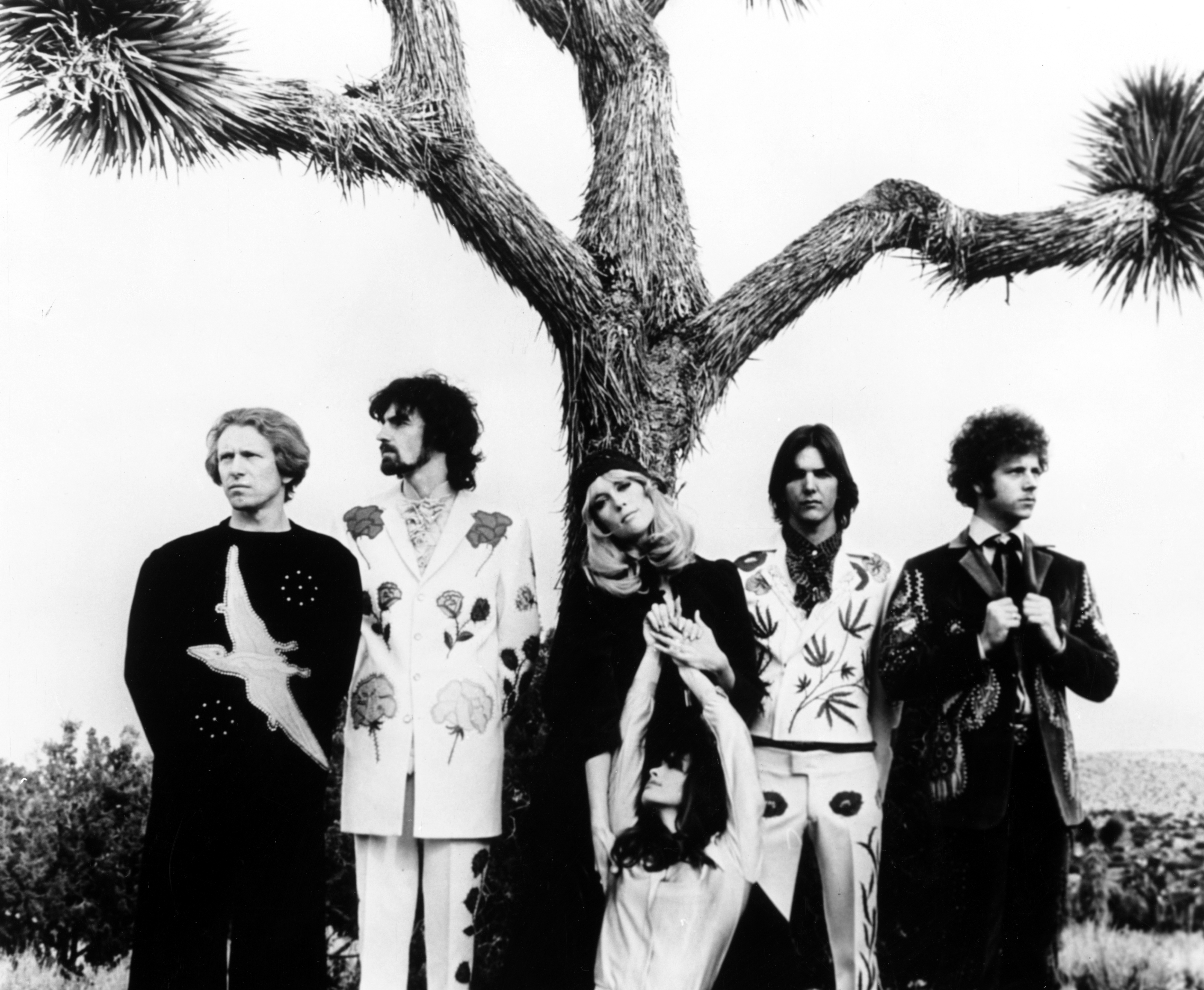 FEBRUARY 7: (L-R) "Sneaky" Pete Kleinow, Chris Ethridge, Gram Parsons and Chris Hillman of the country rock group "The Flying Burrito Brothers" wear Nudie suits designed by Nudie Cohn of Nudie's Rodeo Tailors as they pose for a portrait with 2 female fans in front of a Joshua Tree on February 7, 1969 in Joshua Tree, California.