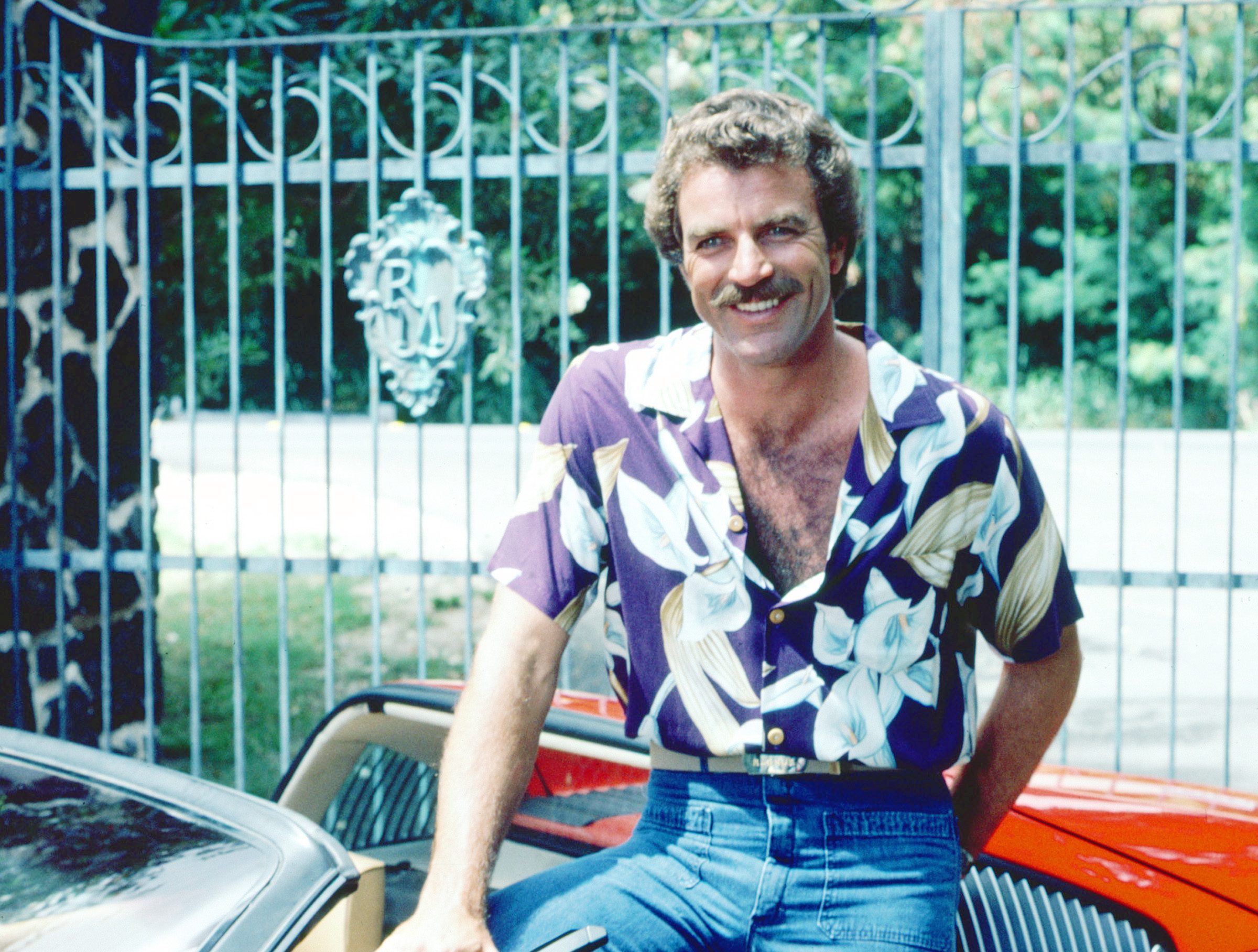 Tom Selleck as the titular investigator in the television series 'Magnum, P.I.', circa 1985. He is posing with his red Ferrari 308. 