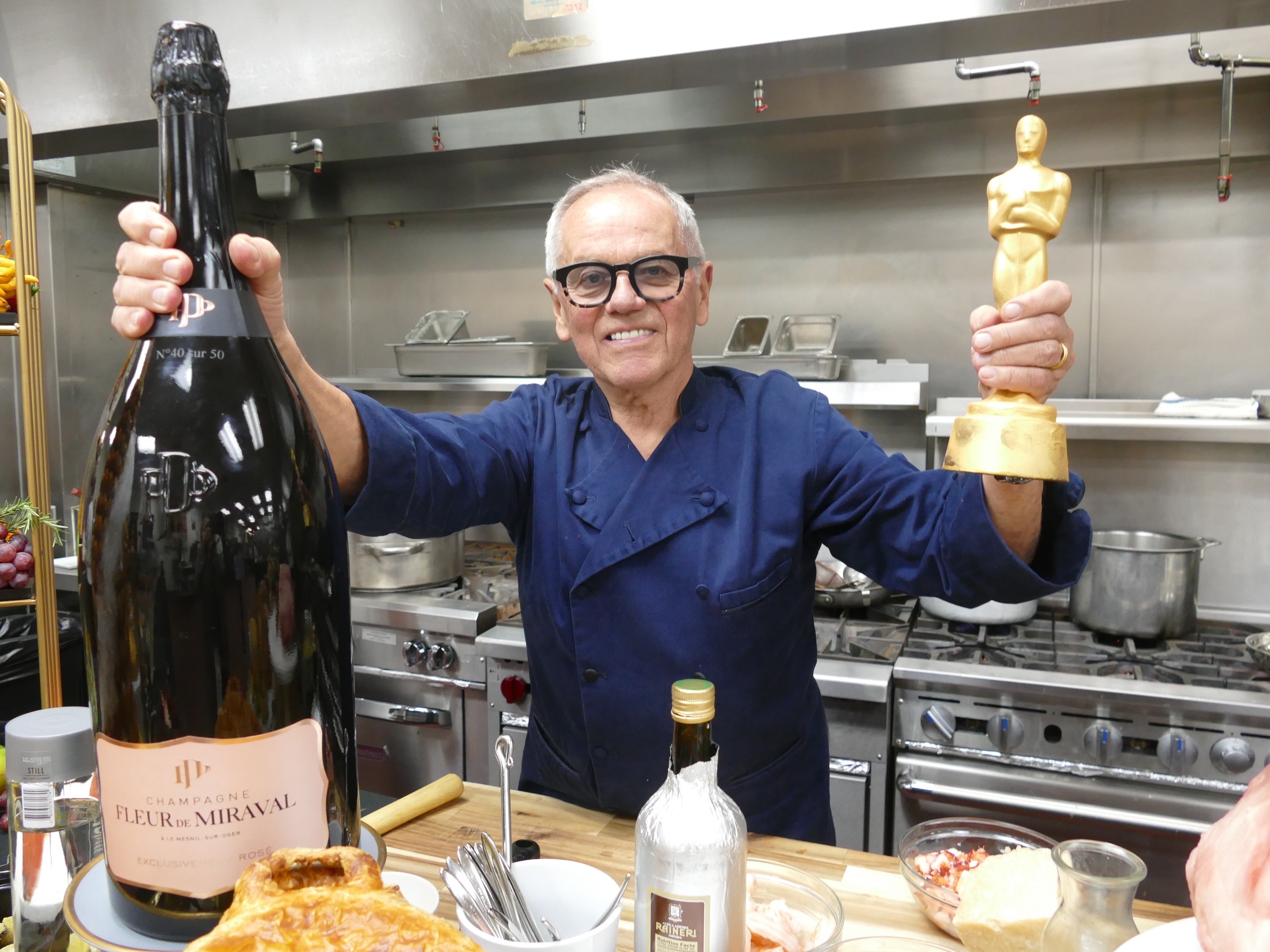 08 March 2023, USA, Los Angeles: Star chef Wolfgang Puck stands in a kitchen with an imitation Oscar statue and a huge bottle of champagne. Puck is serving up food for the 29th time after the Oscar gala for the celebrity guests - this time, too, he has made provisions for the big appetite. (to dpa "Star chef Wolfgang Puck: "Everyone gets an Oscar from me") Photo: Barbara Munker/dpa 