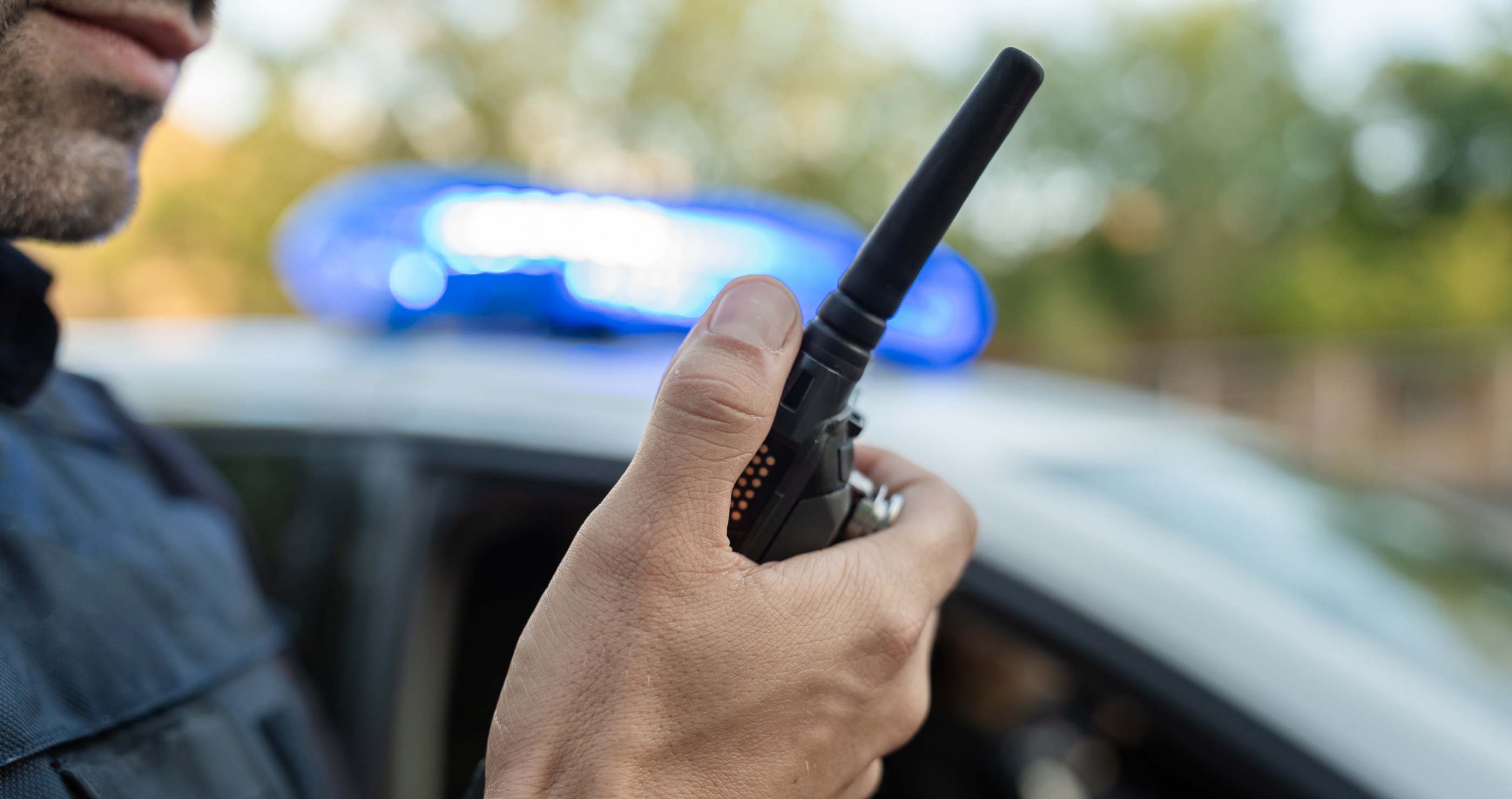 police officer speaking into a walkie talkie with a cop car in the background