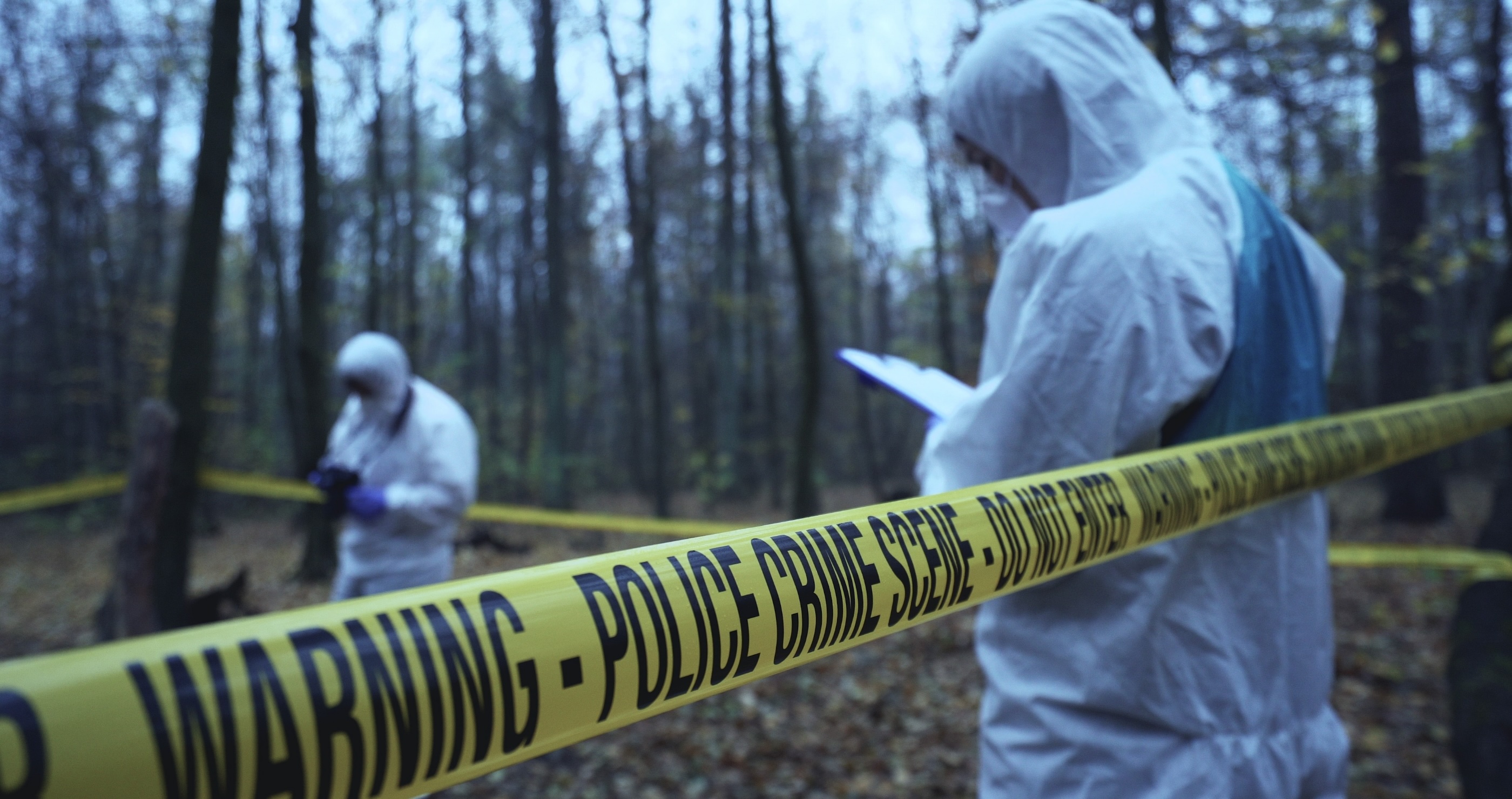 men in hazmat suits behind caution tape in a field