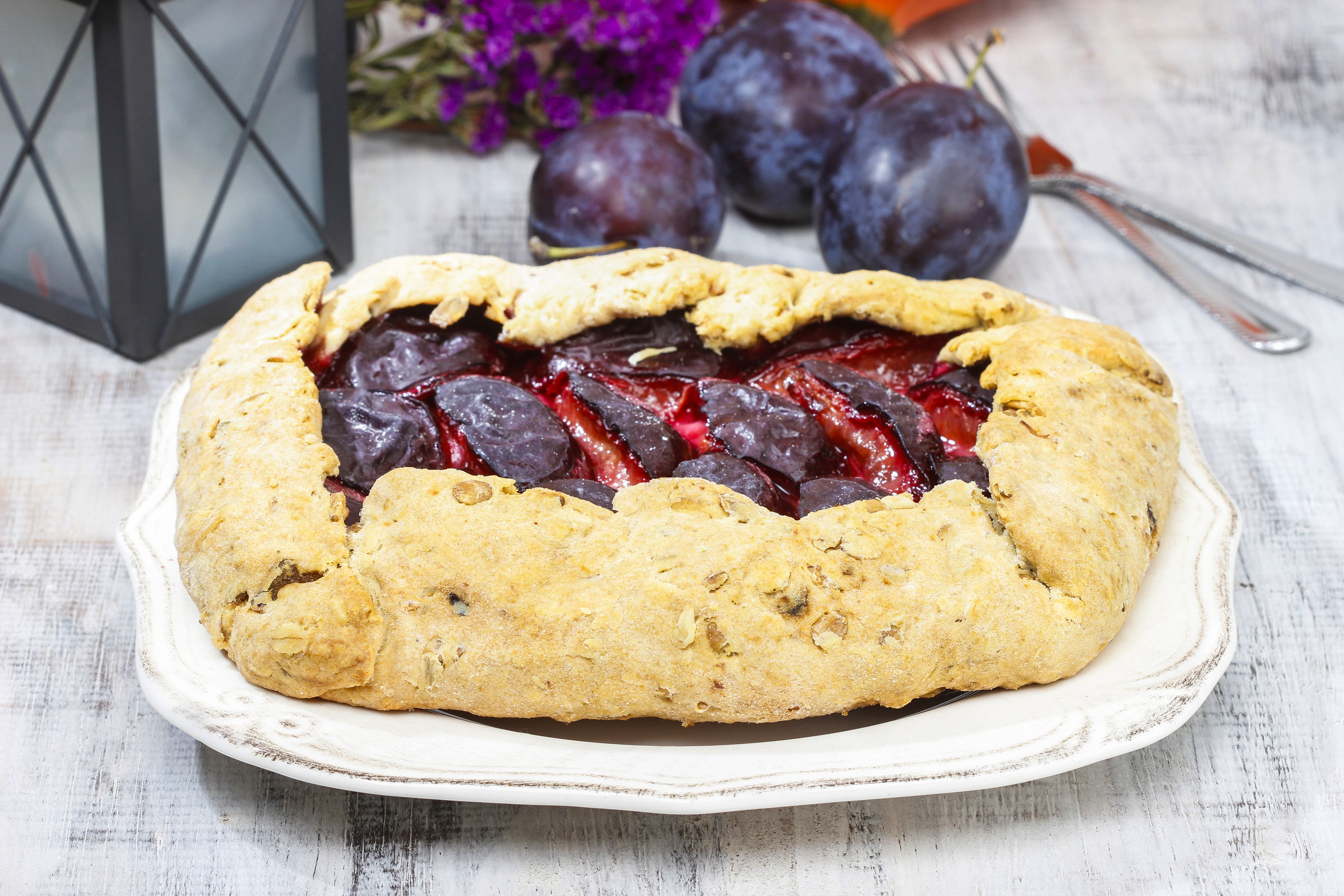Plum galette on wooden table. Raw plums and pumpkins in the back