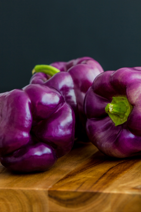 Purple bell peppers, Sweet Pepper Tequila, Capsicum annum, on a wooden board against a dark blue background.  Copy space, selective focus, close up, vertical