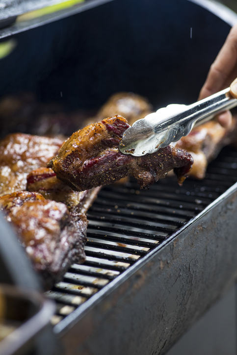 Smoke rising around a slow cooked beef brisket on the grill grates of a smoker barbecue. Grilled spare ribs macro - pork ribs. Lifestyle, food concept.