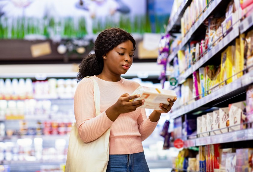 Attractive black woman with tote bag holding food product, buying groceries at supermarket