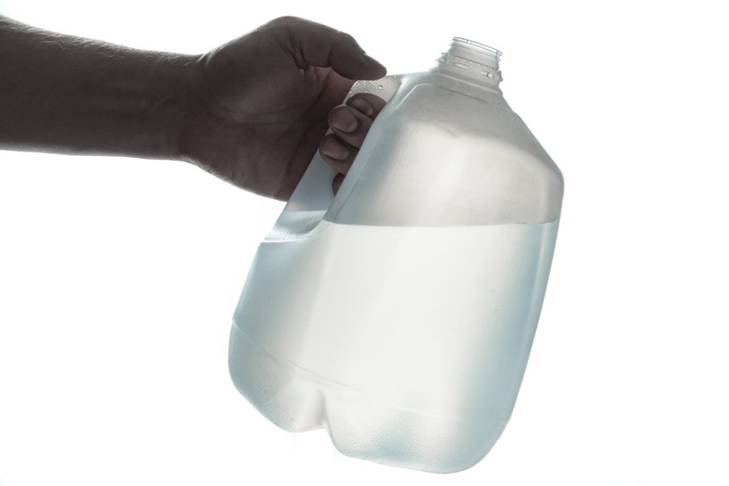 Hand holding 1 gallon plastic bottle of drinking water