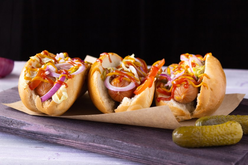 Hot dogs with vegetables, mustard and ketchup on a cutting board, side view Fast food, street food.