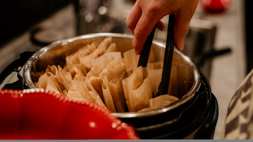 Grabbing tamales from cooker.
