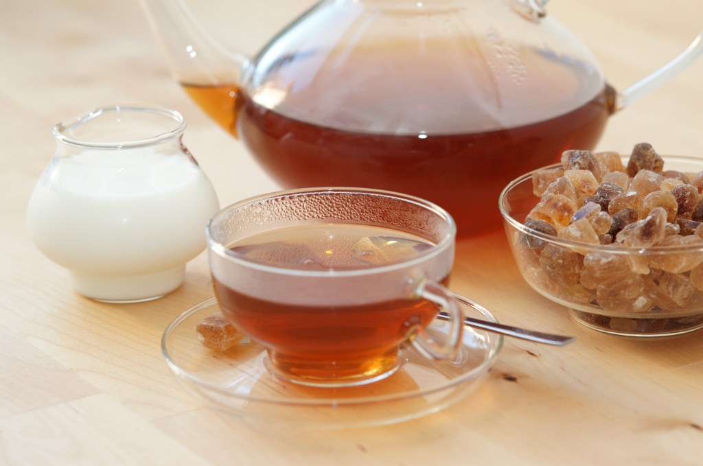 Black tea in a glass with milk in a pot and rock candy sugar