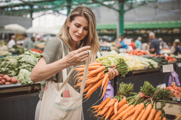 Cheerful woman selecting fresh vegetables in market, everything is fresh and organic