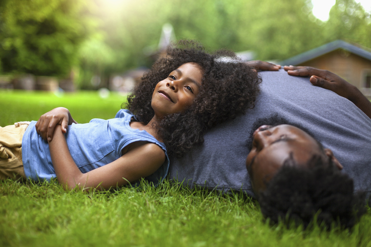 African-American son and father rests on grass at backyard holiday villa