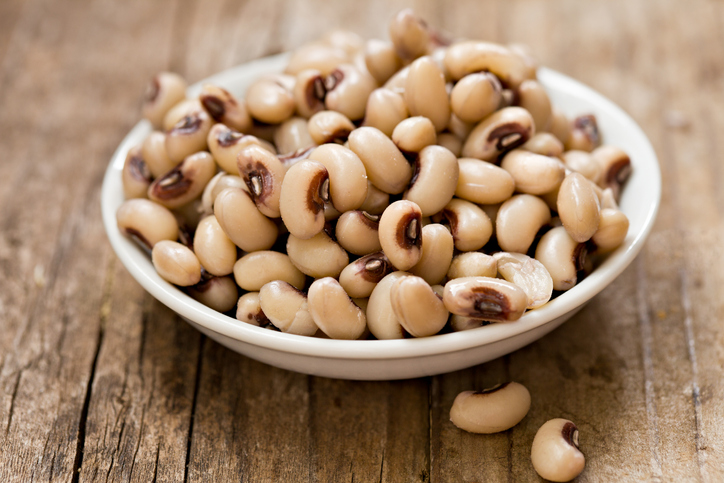 A high angle close up shot of a small white bowl of cooked black eyed peas. Shot on a grungy old wooden table.