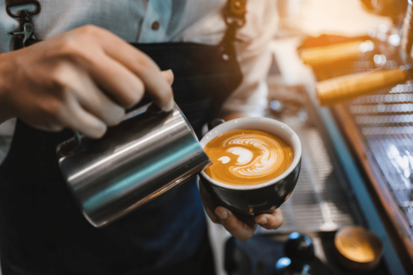 barista pouring milk into coffee