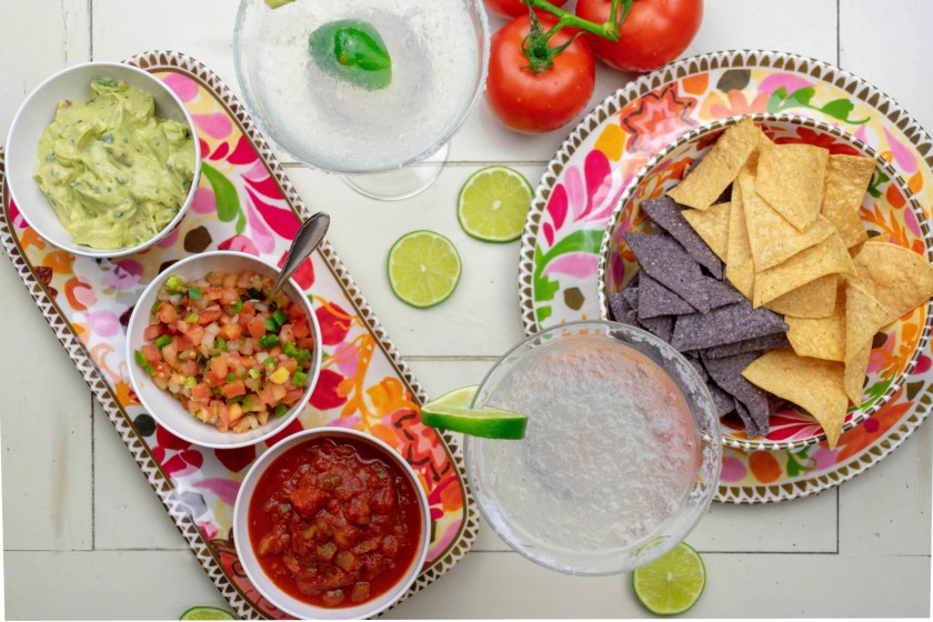 Mexican food flat lay - top view of chips, salsas, fresh ingredients and margaritas